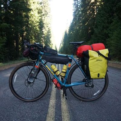 The bike is blue is color and is covered in luggage and water bottle.